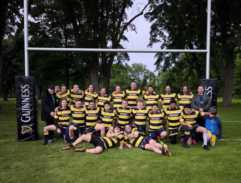 SCS Rugby Team 2025 Gruppenshot einer Rugbymannschaft in gestreiften Trikots vor den Torpfosten in einem Park. Emma von hinten links steht und lächelt.