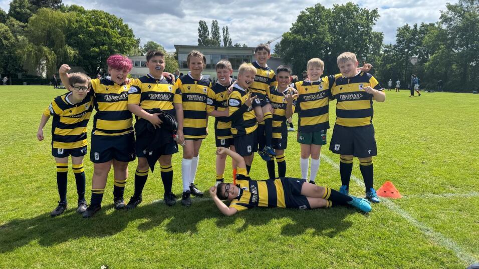 Gruppe von Kindern in gestreiften Rugby-Trikots posiert fröhlich auf einem grünen Rasenfeld.