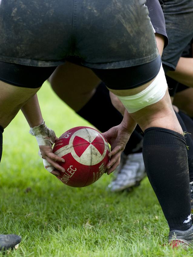 Rugby-Spieler in kniender Position, die einen roten Rugbyball im Gras vorbereiten.