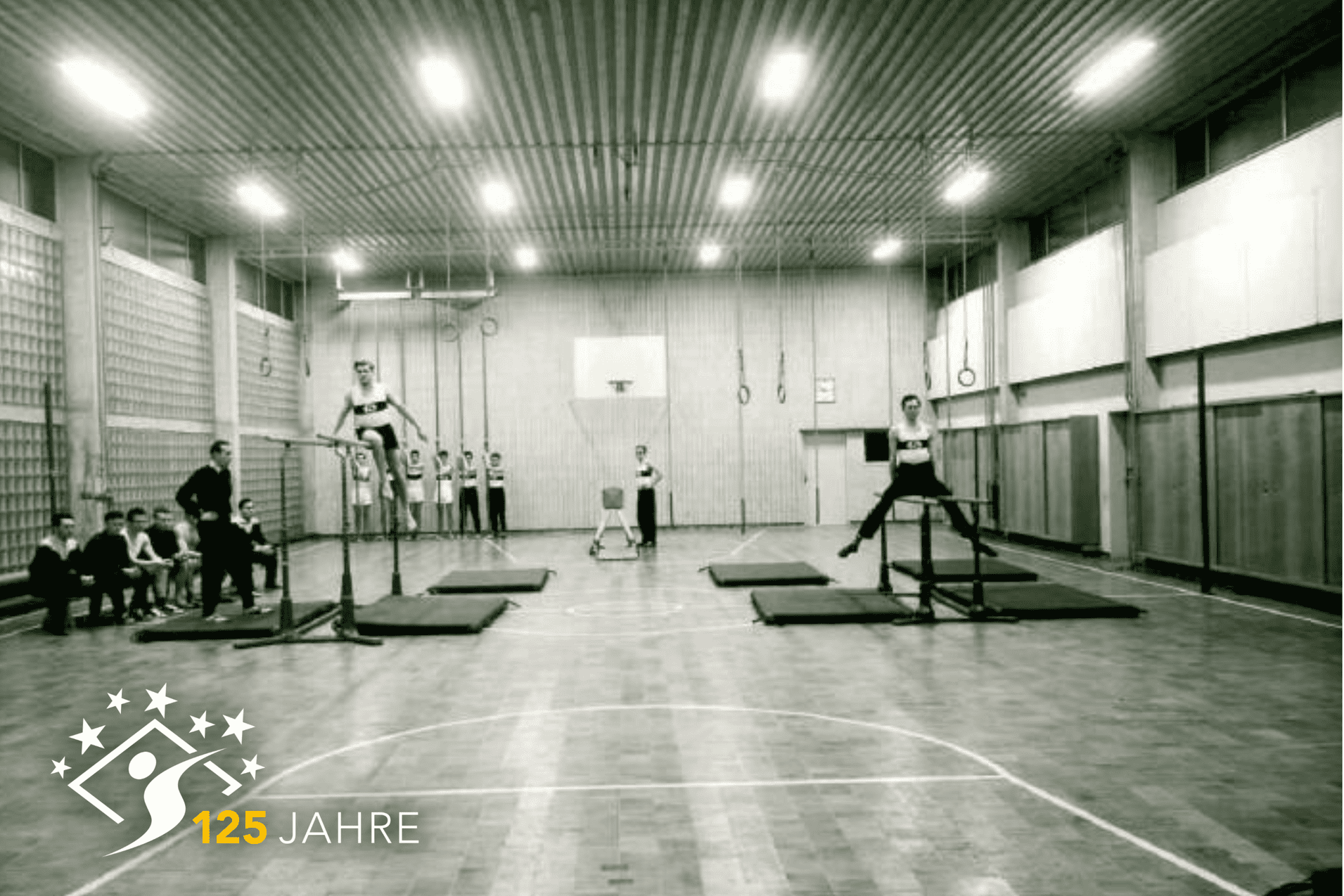 Sporthalle mit Sportlern, die an Turnger&auml;ten trainieren, Zuschauer sitzen auf B&auml;nken im Hintergrund. Schwarz-Wei&szlig;-Foto.