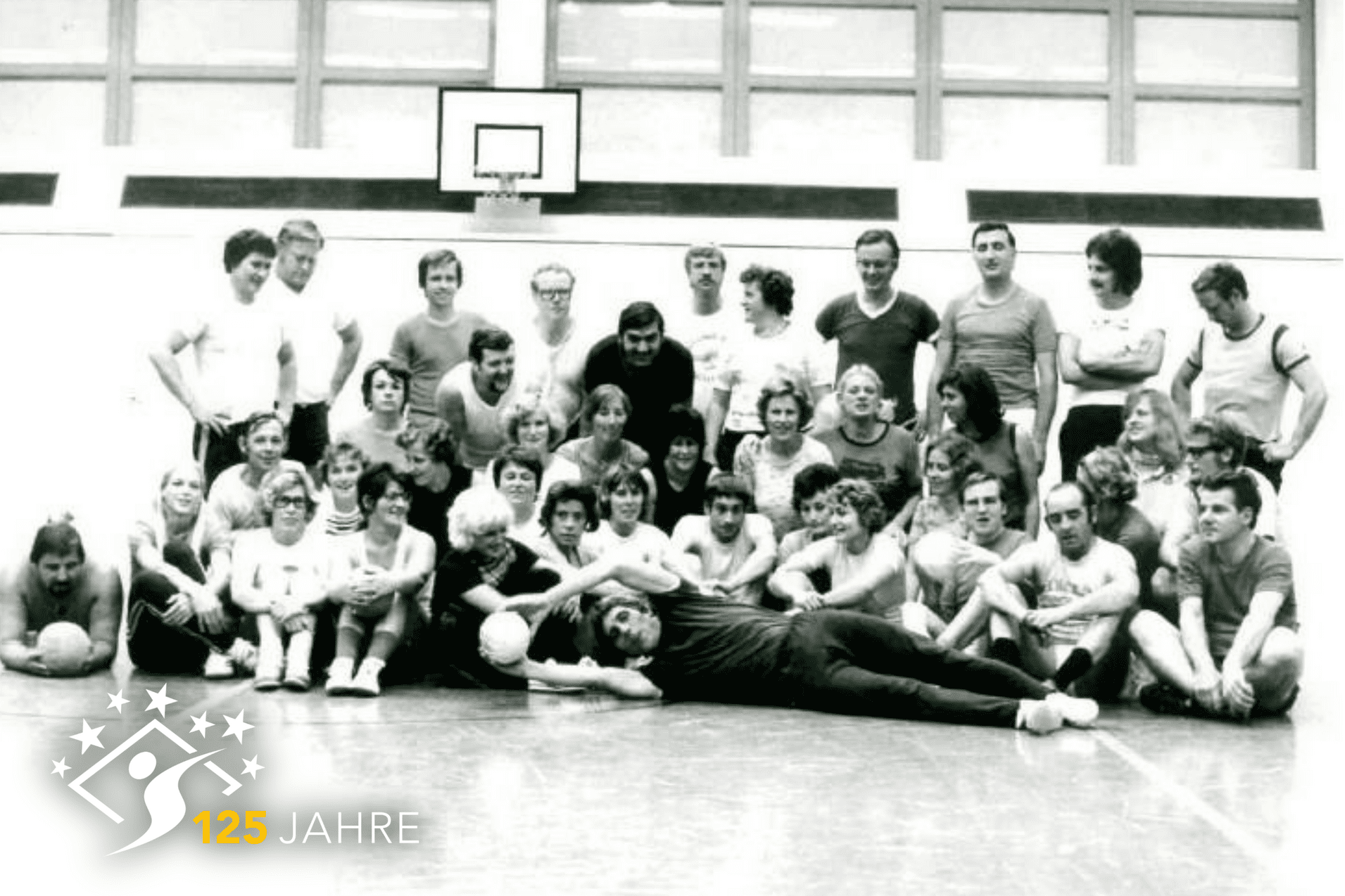 Gruppenfoto von sportlichen Menschen in einer Halle, einige halten B&auml;lle, im Hintergrund ein Basketballkorb.