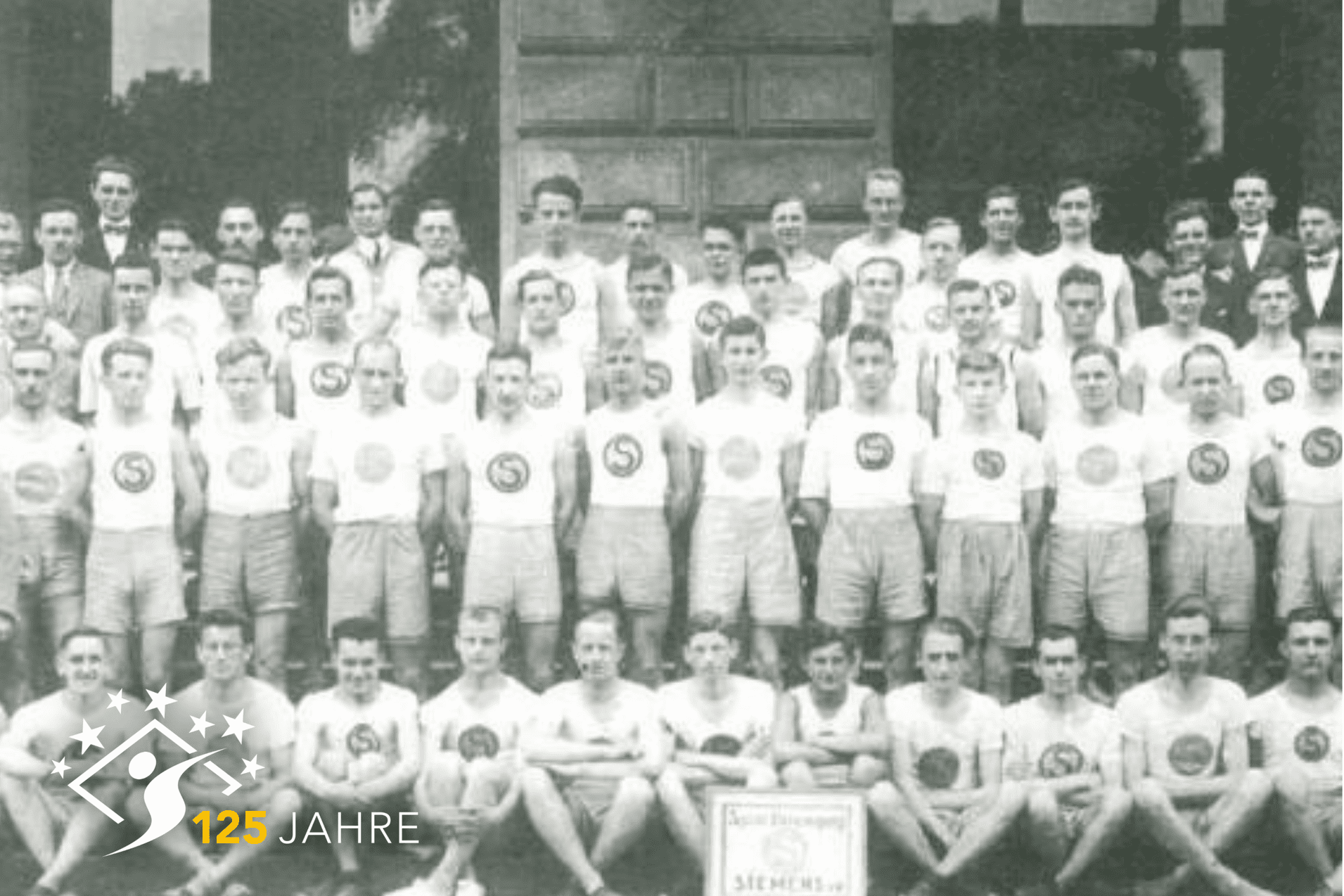 Schwarzwei&szlig;foto einer Sportmannschaft mit einheitlichen T-Shirts und Shorts,gestellt vor einer gro&szlig;en T&uuml;r.
