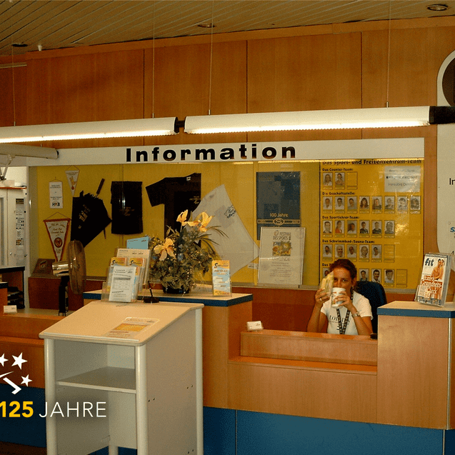 Informationstheke mit Empfangspersonal in einem Gebäude, Informationsmaterialien und Dekoration auf dem Tisch.