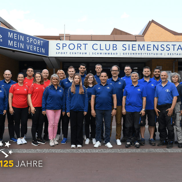 Gruppenfoto von Vereinsmitgliedern des Sport Club Siemensstadt vor dem Vereinsgebäude, gekleidet in blauen und roten T-Shirts.