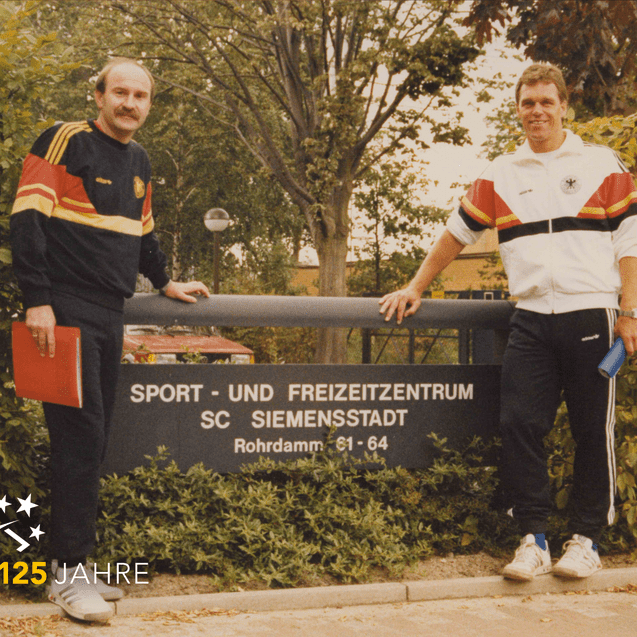 Zwei Männer in Sportbekleidung stehen an einem Schild des Sport- und Freizeit Zentrums SC Siemensstadt.