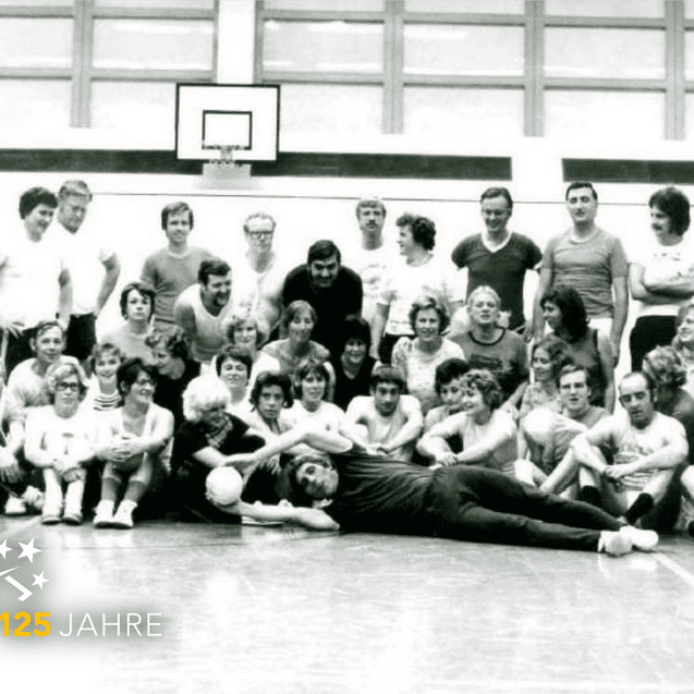 Gruppenfoto von sportlichen Menschen in einer Halle, einige halten B&auml;lle, im Hintergrund ein Basketballkorb.