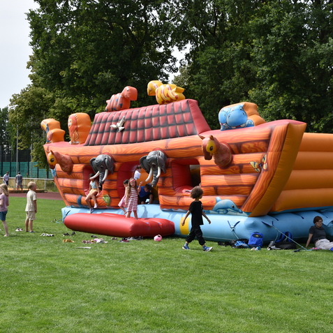 Bunte H&uuml;pfburg in Schiff-Form mit Kindern, die spielen, auf einem gr&uuml;nen Rasenplatz im Freien.