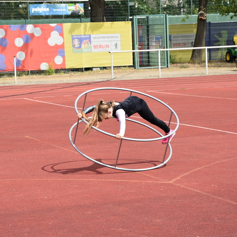 M&auml;dchen balanciert auf zwei Metallreifen auf einer roten Sportfl&auml;che.