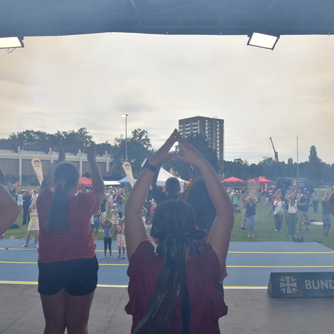 Gruppe von Kindern und Erwachsenen in sportlicher Pose auf einem Eventgel&auml;nde mit bunten Zelten im Hintergrund.