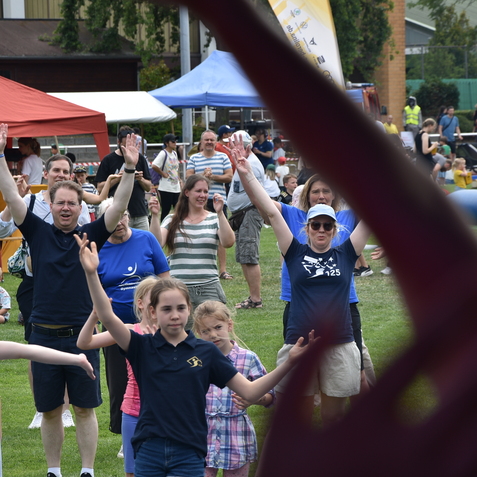 Menschen stehen in einer Reihe und heben die H&auml;nde, um bei einer Veranstaltung im Freien aktiv mitzuwirken.