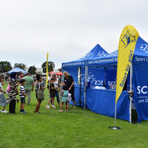 Impression vom Sportfest mit Besuchern am Stand des Sport Club Siemensstadt in Berlin. Bunte Zelte und gr&uuml;ne Wiese.