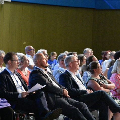 Menschen in einem Innenraum w&auml;hrend einer Veranstaltung; zahlreiche Zuh&ouml;rer blicken aufmerksam nach vorne.