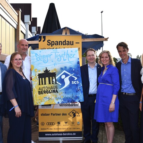 Gruppe von sieben Personen posiert vor einem Plakat mit dem Slogan &bdquo;Stronger Together&ldquo; und dem Logo von Autohaus Berolina.