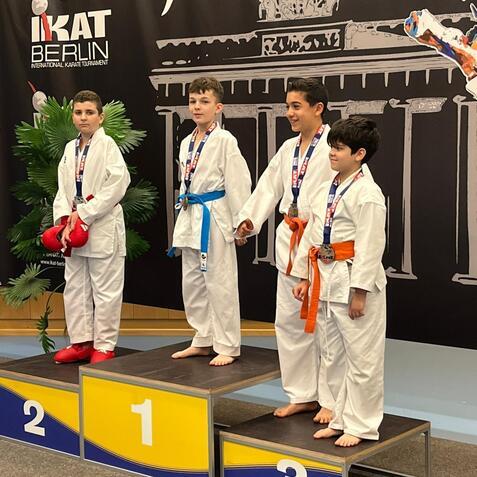 Vier Jungen in Karateanz&uuml;gen stehen auf einem Siegertreppchen beim İKAT Karate-Turnier in Berlin, Medaillen um den Hals.