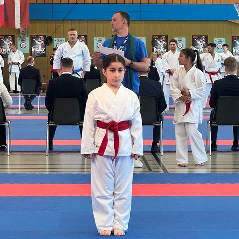 Ein Junge im Karateanzug mit rotem Gürtel steht auf einer blau-roten Matte während eines Wettkampfs.