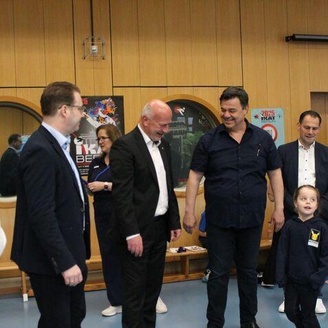 Gruppengespräch in einem Innenraum mit mehreren Personen, darunter ein Kind in einem blauen Hoodie.