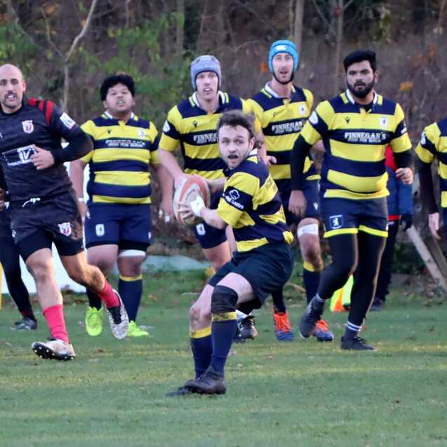 Rugbyspieler in gelb-schwarzen Trikots verfolgt einen Mitspieler mit dem Ball auf dem Spielfeld.