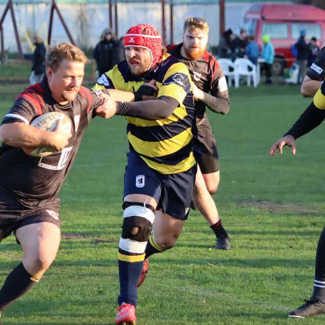 Rugby-Spieler im Wettkampf, einer tr&auml;gt ein schwarzes Trikot, der andere ein gestreiftes, beide k&auml;mpfen um den Ball.