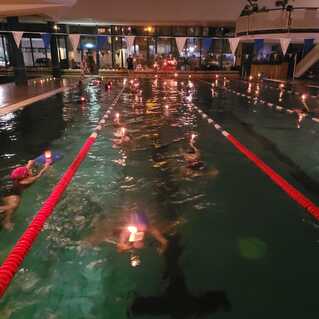 Schwimmbecken mit Teilnehmern, die Kerzen halten, umgeben von ged&auml;mpftem Licht und festlicher Dekoration.