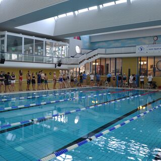 Schwimmbecken mit Teilnehmern an einem Wettkampf, die in einer Reihe am Beckenrand stehen.