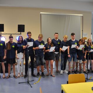 Gruppe von Jugendlichen in blauen T-Shirts singt vor Mikrofonen und B&uuml;hnenbeleuchtung. помещение="{{заметить}}"