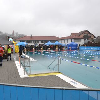 Blick auf ein Schwimmbad mit Rettungskr&auml;ften, Zelten und Zuschauern an einem grauen, regnerischen Tag.