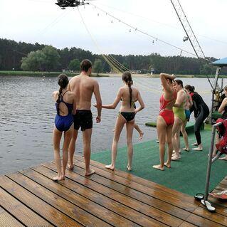 Gruppe von Jugendlichen in Badebekleidung am Ufer eines Gew&auml;ssers, bereit zum Wassersport.