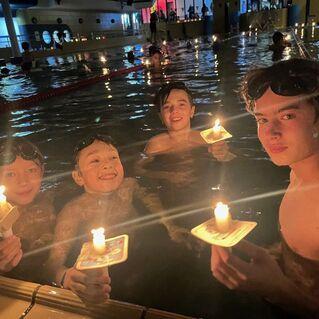 Vier Kinder stehen im Wasser eines Schwimmbades und halten jeweils eine Kerze in der Hand.