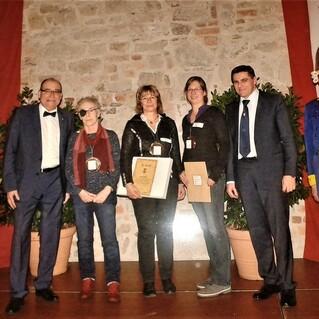 Sechs Personen in formeller Kleidung stehen auf einer B&uuml;hne vor einer Steinwand, einige halten Urkunden in den H&auml;nden.