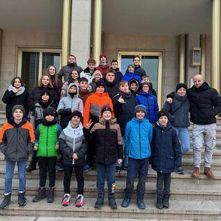 Gruppe von Jugendlichen in Winterkleidung posiert auf den Stufen eines Geb&auml;udes. Pr&auml;senz von 26 Personen, teils l&auml;chelnd.