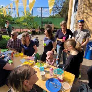Gruppe von Menschen bei einem Fest unter Sonnenschein, sitzend an einem Tisch mit Essen und Getränken.