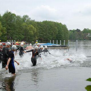 Gruppenschwimmen mit Wettkampfschwimmern in Neoprenanzügen, die ins Wasser eintauchen und Spritzer erzeugen.