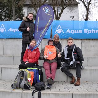 Gruppe von vier Personen sitzt auf einer Treppe, umgeben von Bannern der Marke Aqua Sphere.