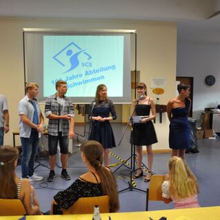 Event zur Feier von 100 Jahren Schwimmabteilung, mit mehreren Sprechern und Publikum in einem festlichen Raum.