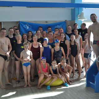 Gruppenfoto von Schwimmern unterschiedlicher Altersgruppen in einem Schwimmbad, vor einer blauen Bannerwand posierend.