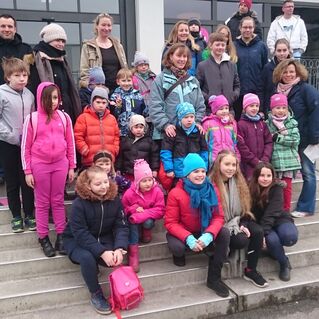 Gruppe von Kindern und Erwachsenen posiert auf Treppenstufen vor einem Gebäude, in winterlicher Kleidung und mit bunten Mützen.