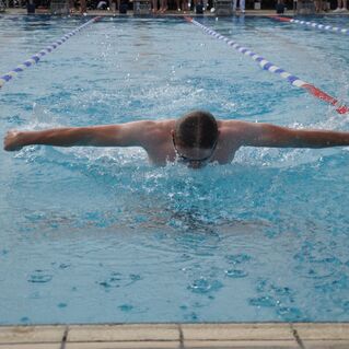 Schwimmer im Schmetterlingsstil, taucht mit gestreckten Armen durch das Wasser in einem Schwimmbecken.