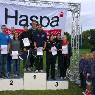 Siegerpodest mit neun Personen, die Urkunden halten, im Hintergrund Banner der Haspa und Zuschauer im Freien.