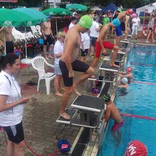 Schwimmer stehen an Startblöcken am Beckenrand eines Wettbewerbs, während Zuschauer und Trainer beobachten.