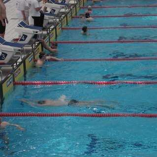 Schwimmer in einem Stadionbecken trainieren, während einige an der Beckenrande ruhen oder sich vorbereiten.