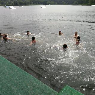 Gruppe von Schwimmern in einem See, umgeben von Wasser und einem grünen Steg im Vordergrund.
