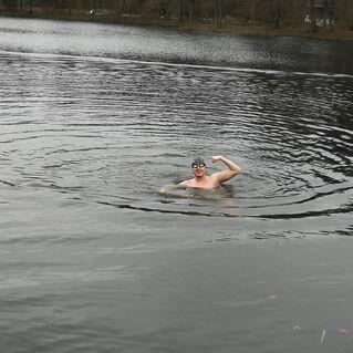 Mann schwimmt im See und zeigt muskulöse Pose, während sich Wellen um ihn herum bewegen.
