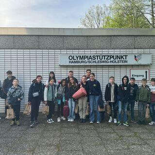 Gruppe von Jugendlichen vor dem Olympiastützpunkt Hamburg/Schleswig-Holstein mit Eingangsschild im Hintergrund.