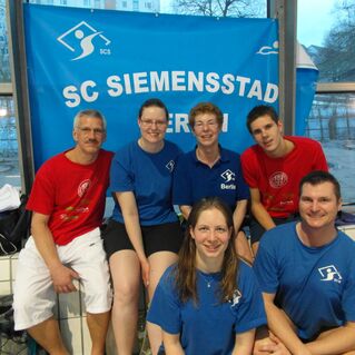 Gruppe von sechs Schwimmers*innen in blauen und roten T-Shirts vor einem Banner des SC Siemensstadt.