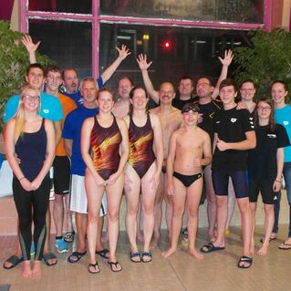 Gruppennaufnahme von Schwimmern in Badebekleidung, umgeben von Pflanzen in einem Hallenbad. Alle lächeln und posieren.