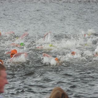 Gruppenschwimmen im Wasser mit Sportlern in bunten Schwimmkappen und Spritzwasser.