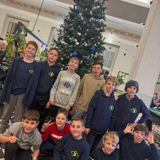 Gruppe von zehn Jungen in blauen Sweatshirts vor einem Weihnachtsbaum in einem hellen Raum.