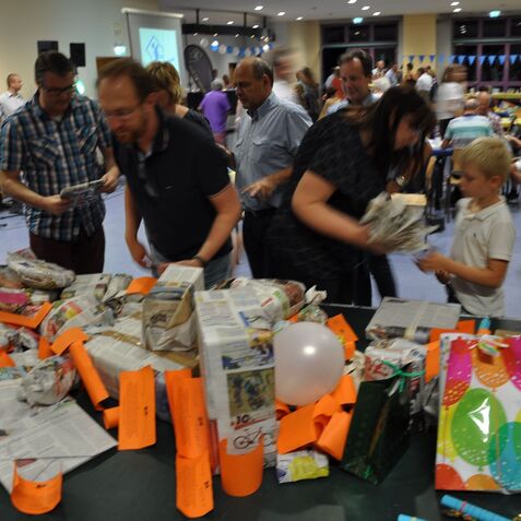 Menschen versammeln sich um einen Tisch, der mit eingewickelten Geschenken und bunten Zetteln bedeckt ist.