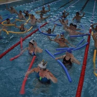 Gruppentraining im Schwimmbecken mit Teilnehmern, die auf Schwimmnudeln stehen und Bewegungen ausführen.