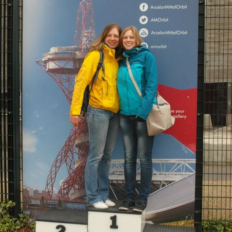Zwei Frauen stehen auf einer Treppe mit den Zahlen 1, 2 und 3, vor einem Hintergrund des ArcelorMittal Orbit.